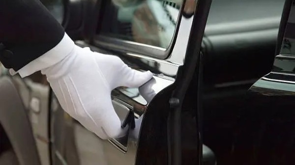 a gloved hand holding open the door of a luxury car